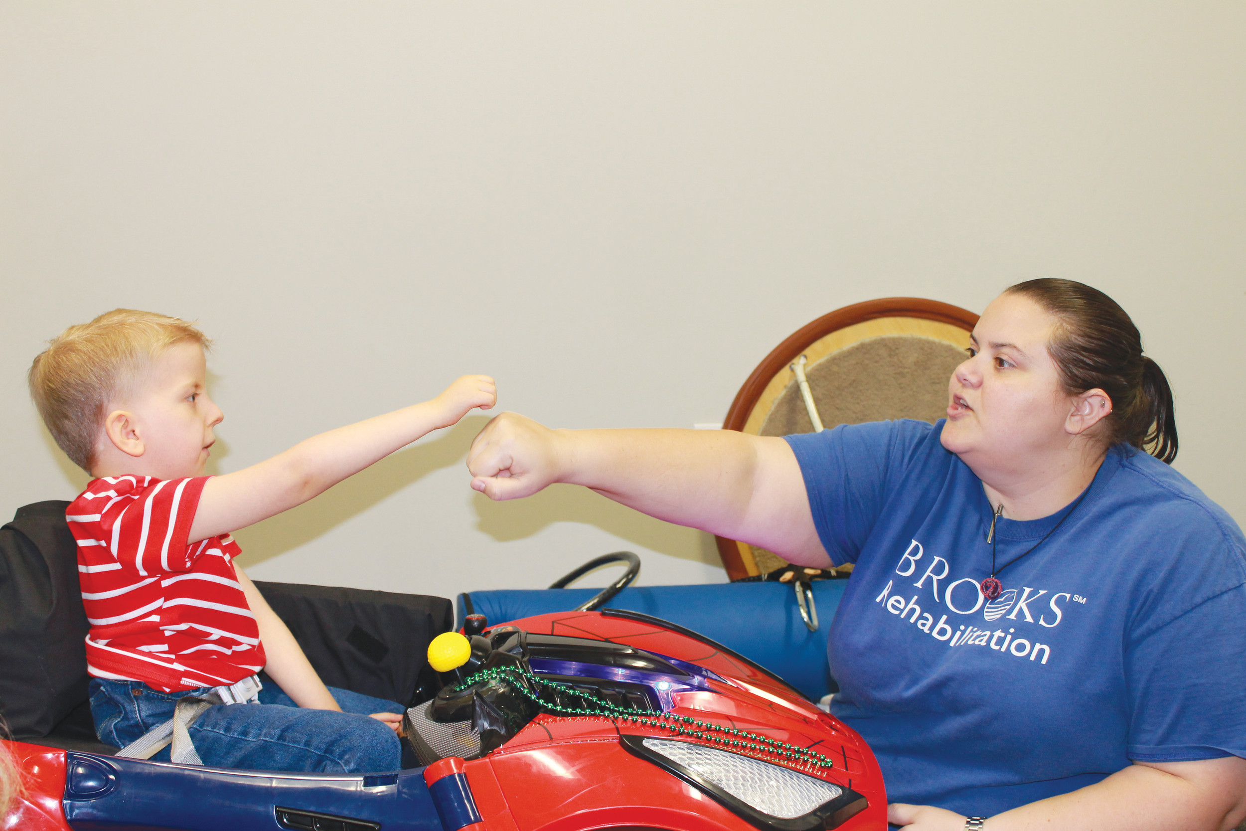 James Bujold, center, prepares to operate a modified Power Wheels car during a recent therapy session with help from his father, Jim Bujold, left, and physical therapist, Kelly Kelaney.